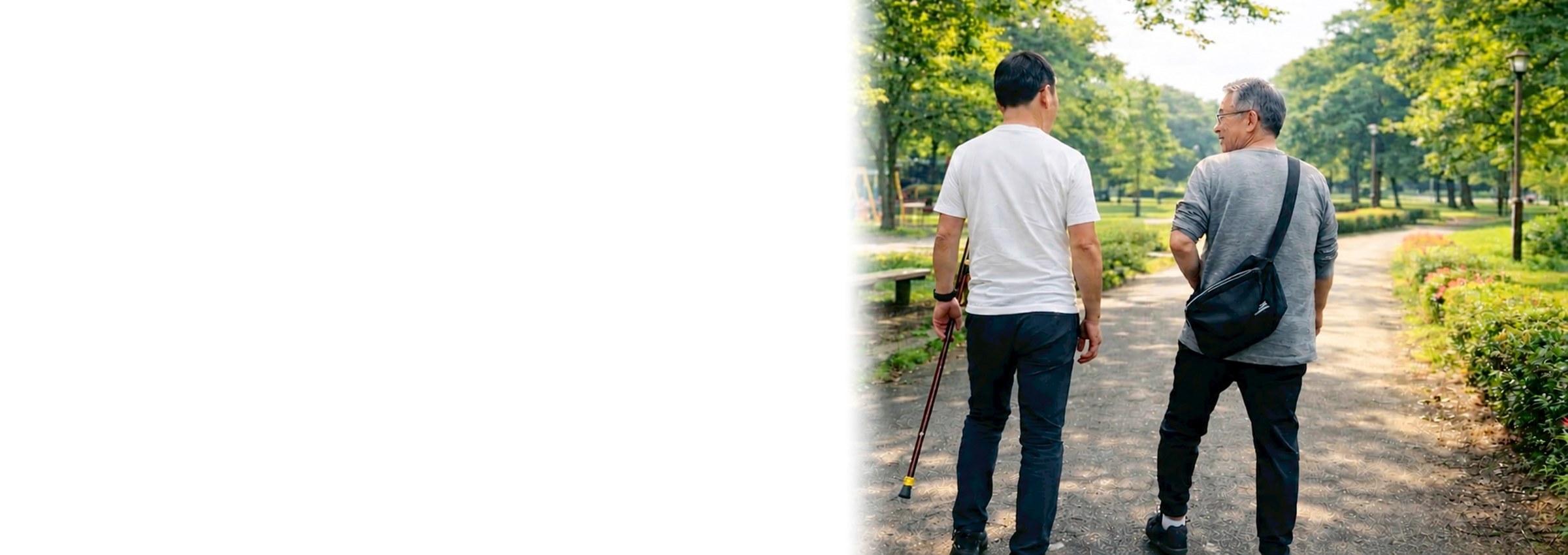 杖をついた男性と付き添いの男性が、公園の並木道を並んで歩いている